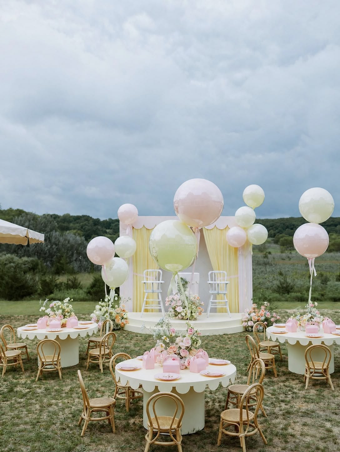 Pastel-styled kids' party table set outdoors with balloon garland and child-sized chairs