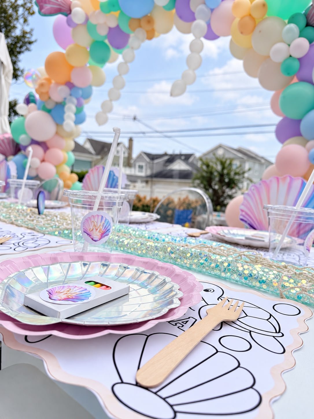 Iridescent shell plates and a coloring placemat set at a child's place at a mermaid party table